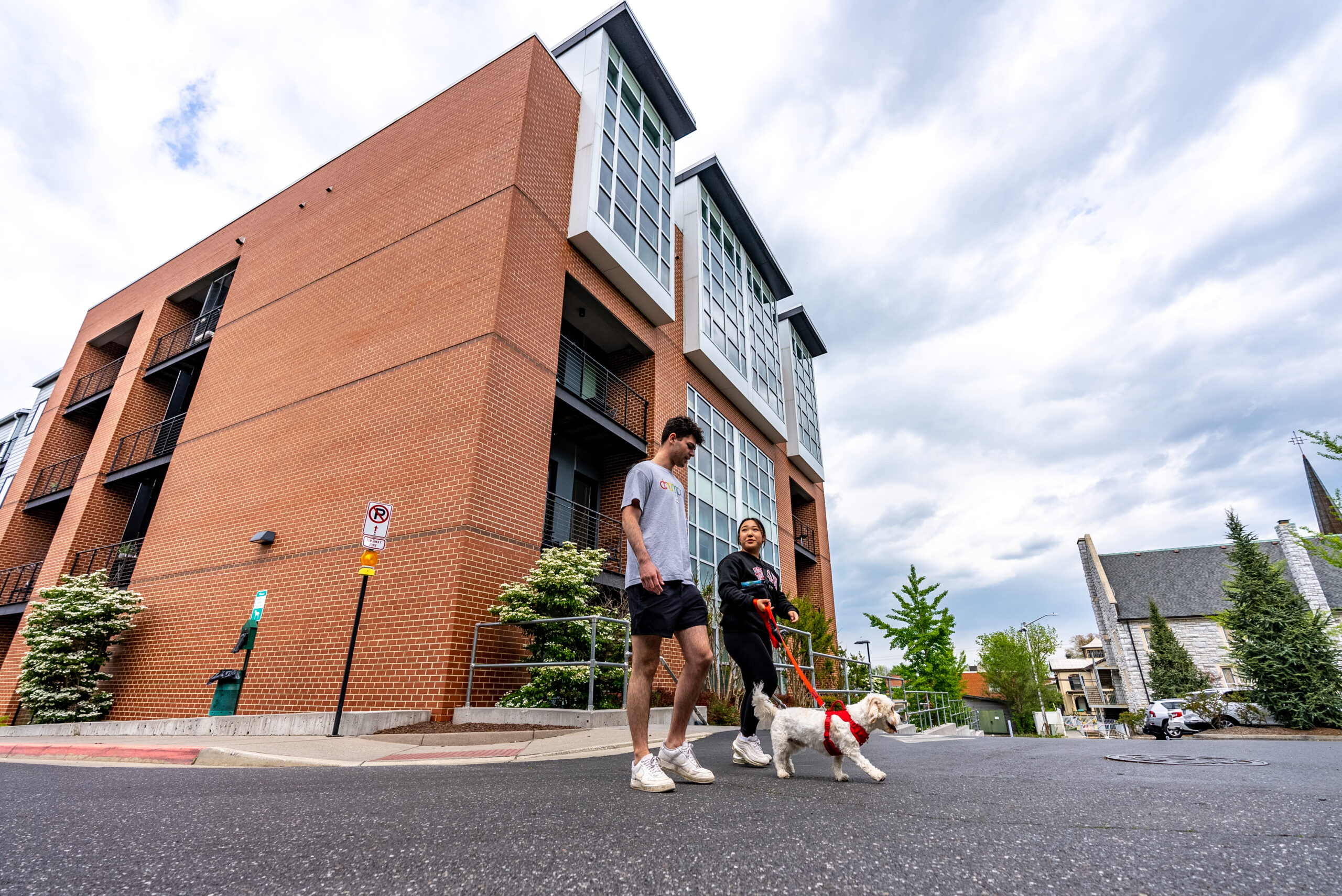 JMU students moving into off-campus housing in Harrisonburg, preparing their apartment to avoid security deposit deductions. Two young adults walk a dog in front of the Urban Exhange Building in Harrisonburg.